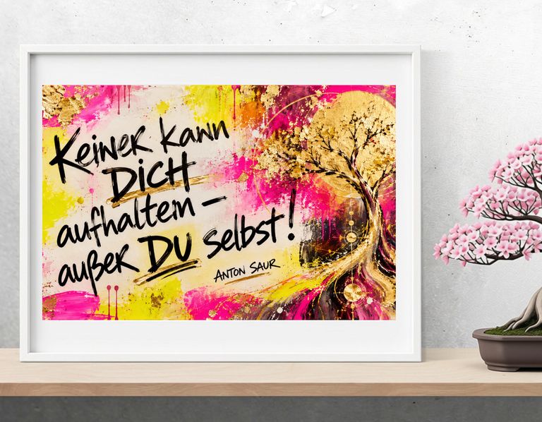 Ein gerahmtes buntes Bild mit dem Schriftzug "Keiner kann Dich aufhalten – außer Du selbst!" von Anton Saur, auf einem Tisch neben einer kleinen blühenden Bonsai-Pflanze.